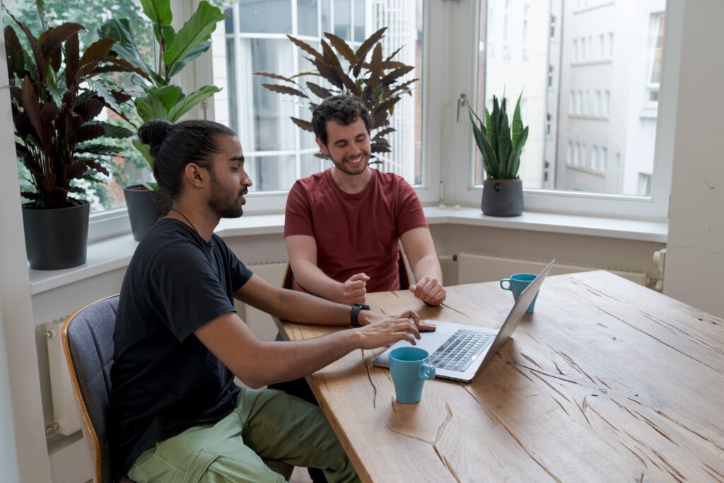 Two men sitting on a desk looking at a laptop